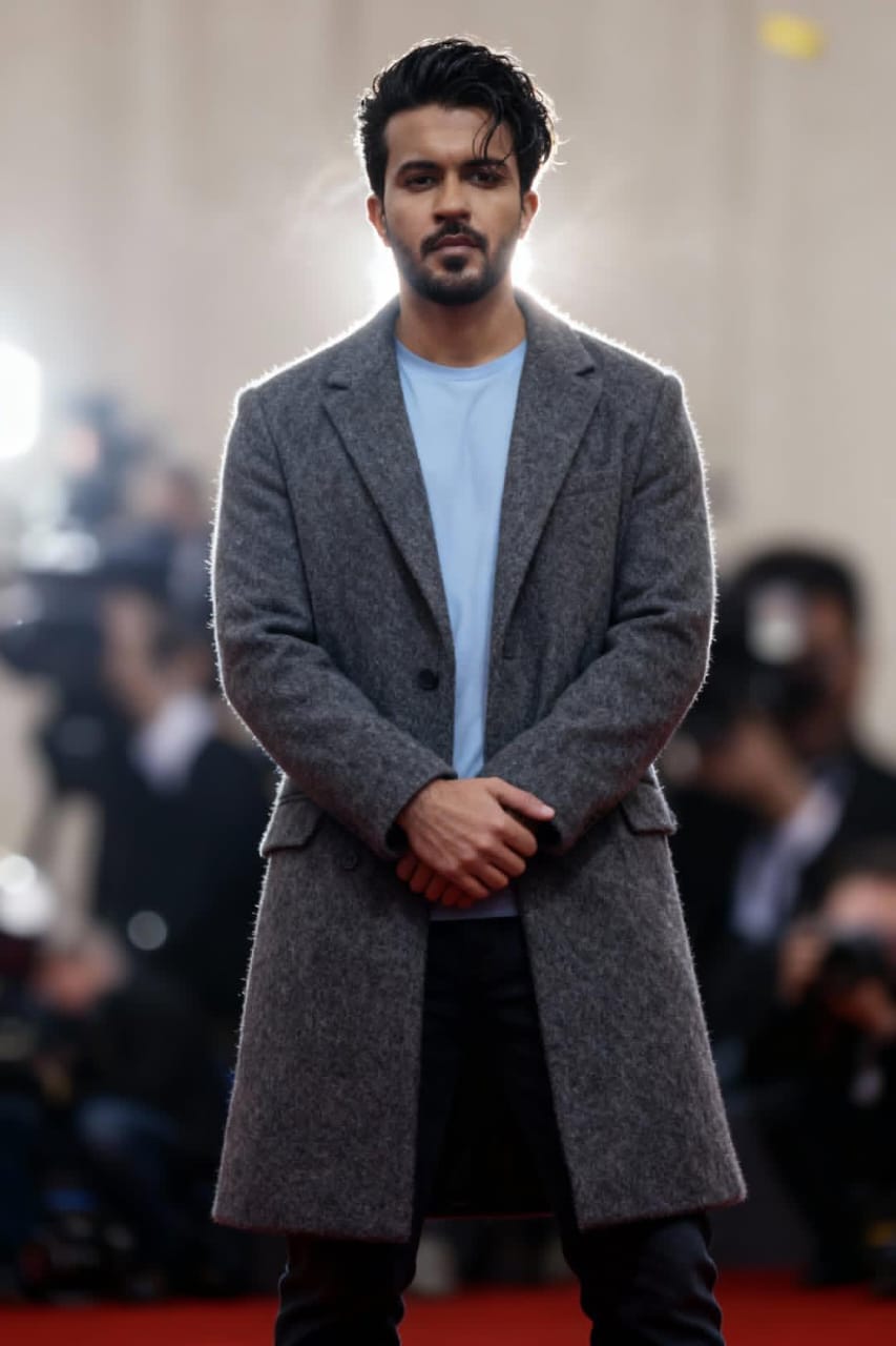 A stylish young man posing on the red carpet in a gray winter coat with a casual blue shirt, ideal for modern men's fashion inspiration.